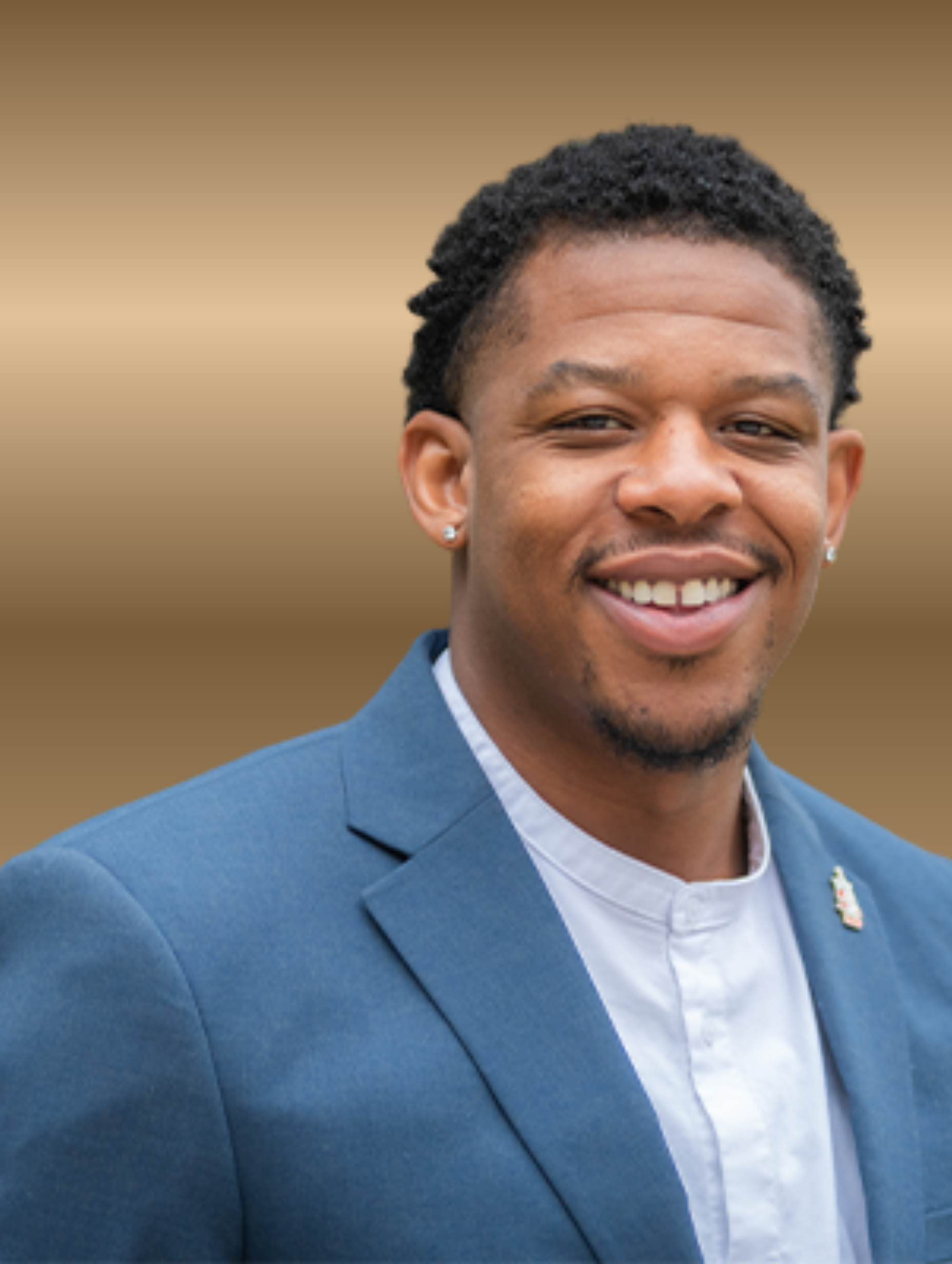 Man in blue blazer and open-collar shirt smiles, set against a golden background.