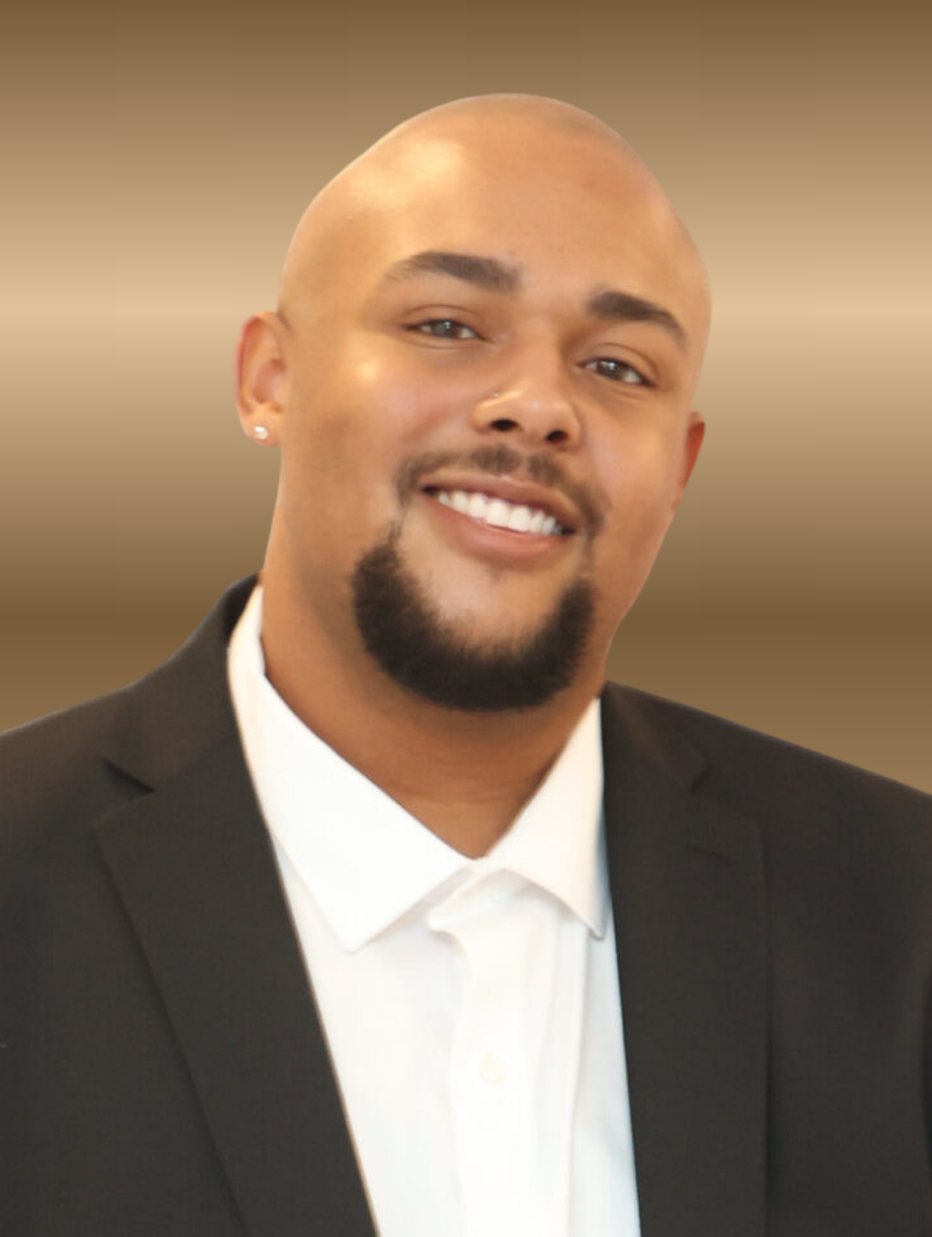Bald man, black suit, white shirt, smiling, goatee, neutral background.