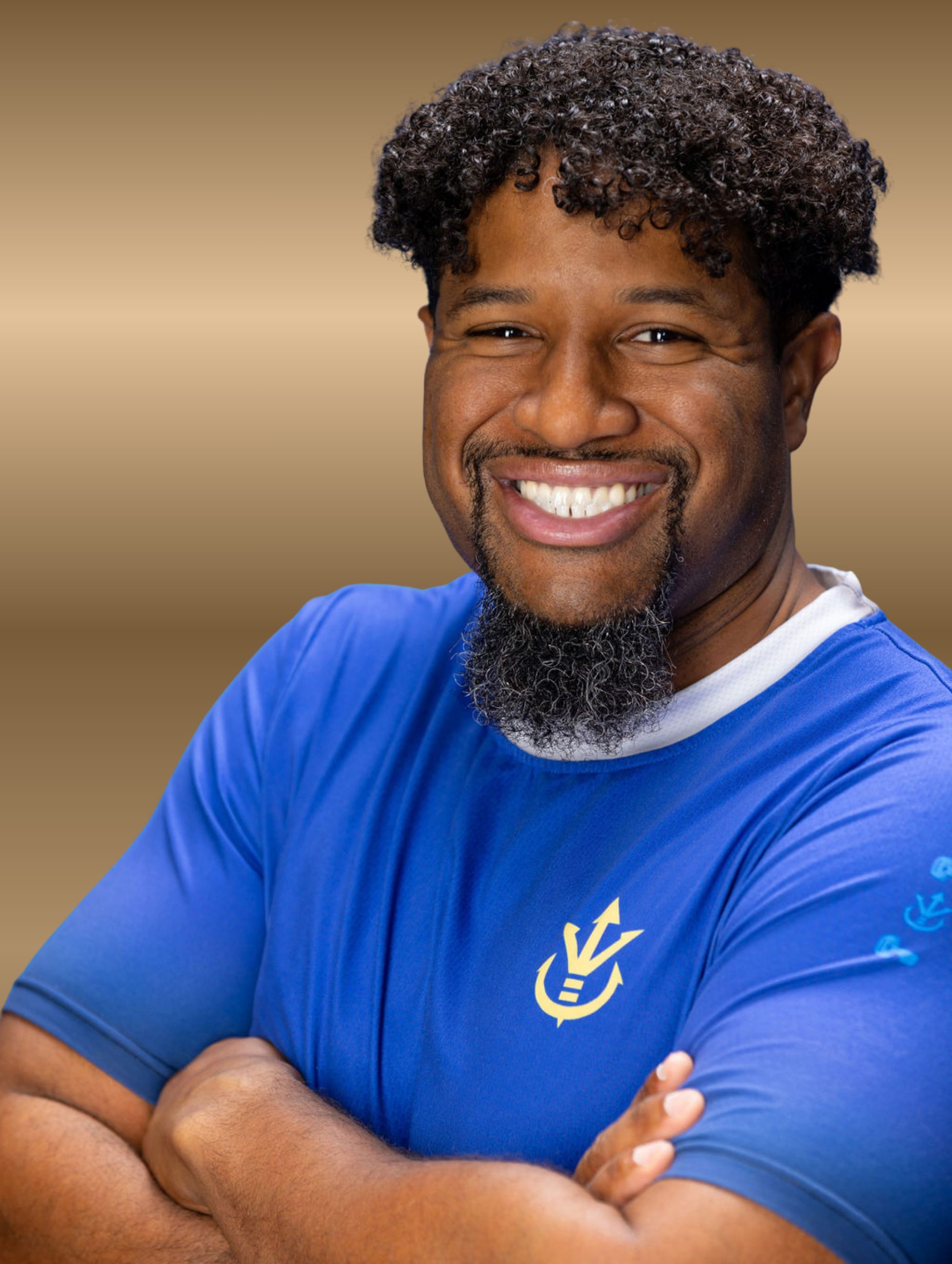 Man with afro, smiling, arms crossed, wearing a blue shirt with a logo, against a gold gradient background.