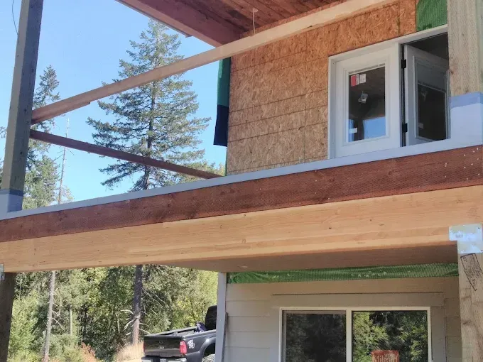 Construction of a building with a balcony; exterior view. Wood beams, door, and windows are visible.