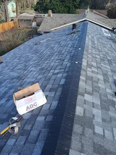 A roof with asphalt shingles, partially replaced. Cardboard box and tools sit nearby.