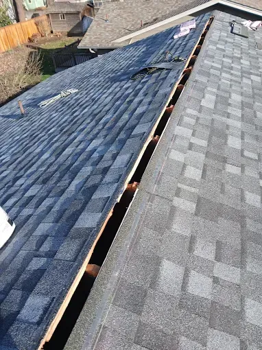 Roof with dark blue and gray shingles, some removed. Gutter area exposed, showing wood.
