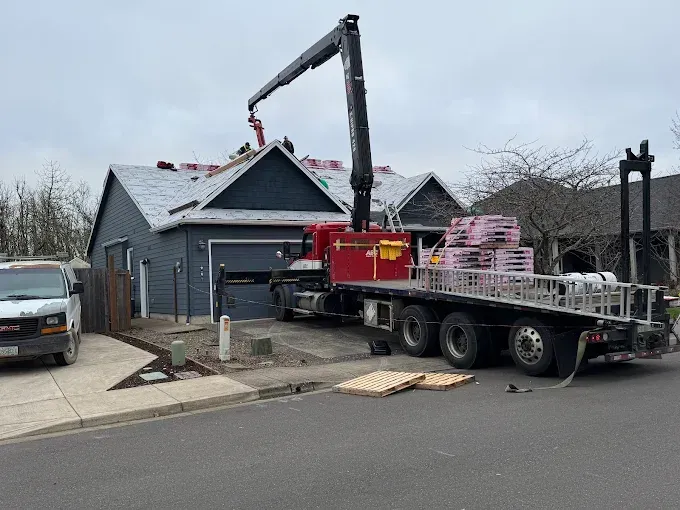 Roofing truck with crane lifting materials to a house roof. Workers on the roof. Cloudy day.