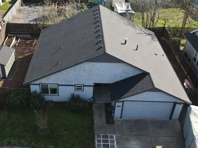 Aerial view of a gray house with a dark gray roof, driveway, and front lawn.