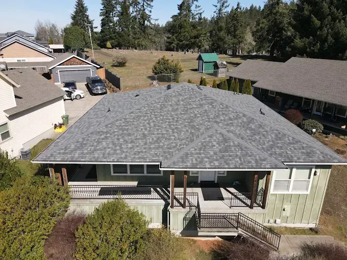 Aerial view of a green house with gray roof, porch, and a driveway with cars.