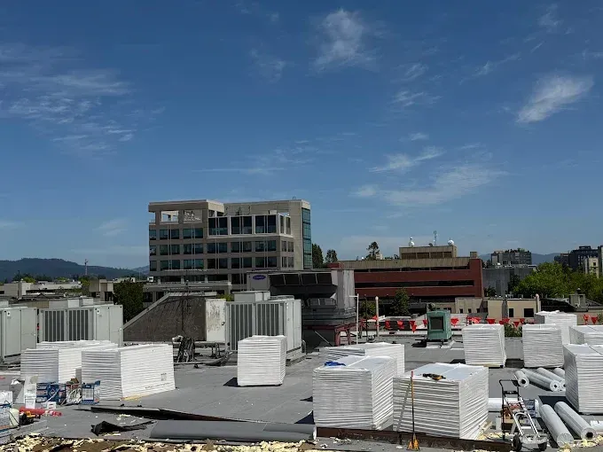 Rooftop view of commercial building under construction with stacked white insulation and equipment; blue sky in background.