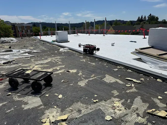 A flat commercial rooftop being worked on with old roofing debris and new roofing material visible.
