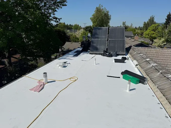 White flat roof with solar panels, a pipe, and tools on a sunny day.