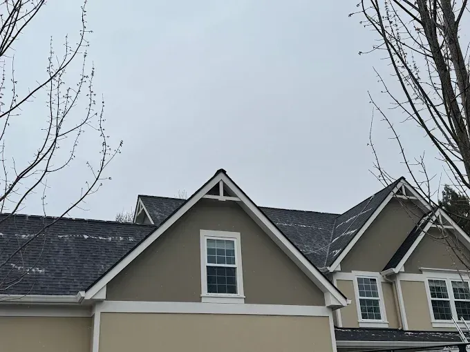 House exterior with dark roof and two triangular dormers, under a cloudy sky.
