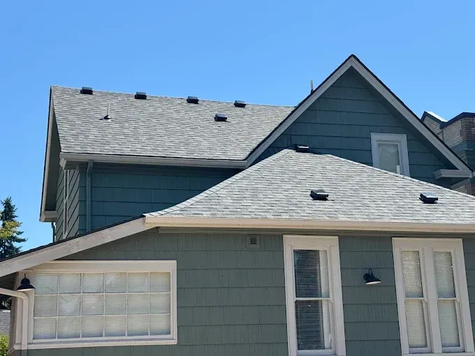 Blue-green house with gray shingled roofs and blue sky.