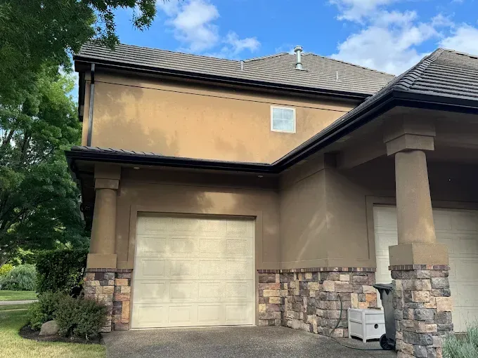 Tan two-story house with stone accents, garage door, and black trim under a blue sky.