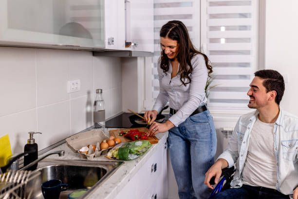 A man in a wheelchair is cooking with a woman in the kitchen.