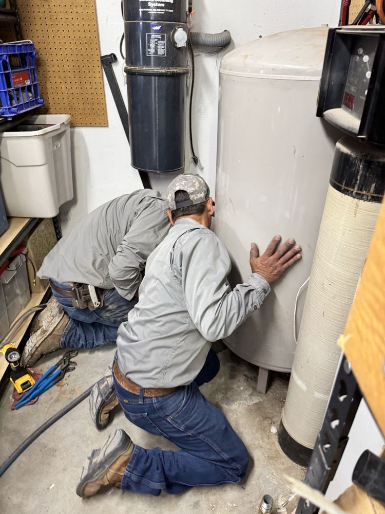 Two people inspecting a large, cylindrical tank in a utility room. One is touching the tank.