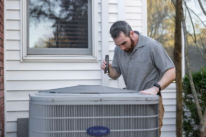 Man inspecting an AC unit with a flashlight outside a building.