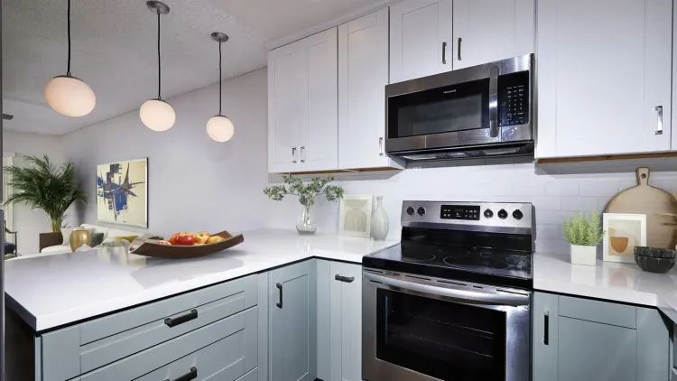 Modern kitchen with gray and white cabinets, stainless steel appliances, and globe pendant lights.