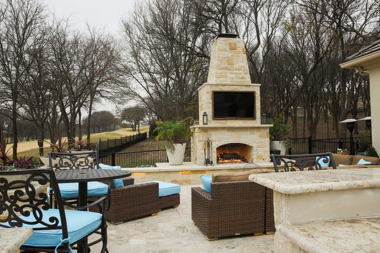 A patio with a fireplace, chairs, a table and a television.