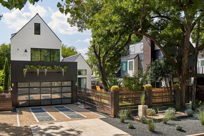 A white house with a black garage door is surrounded by trees.