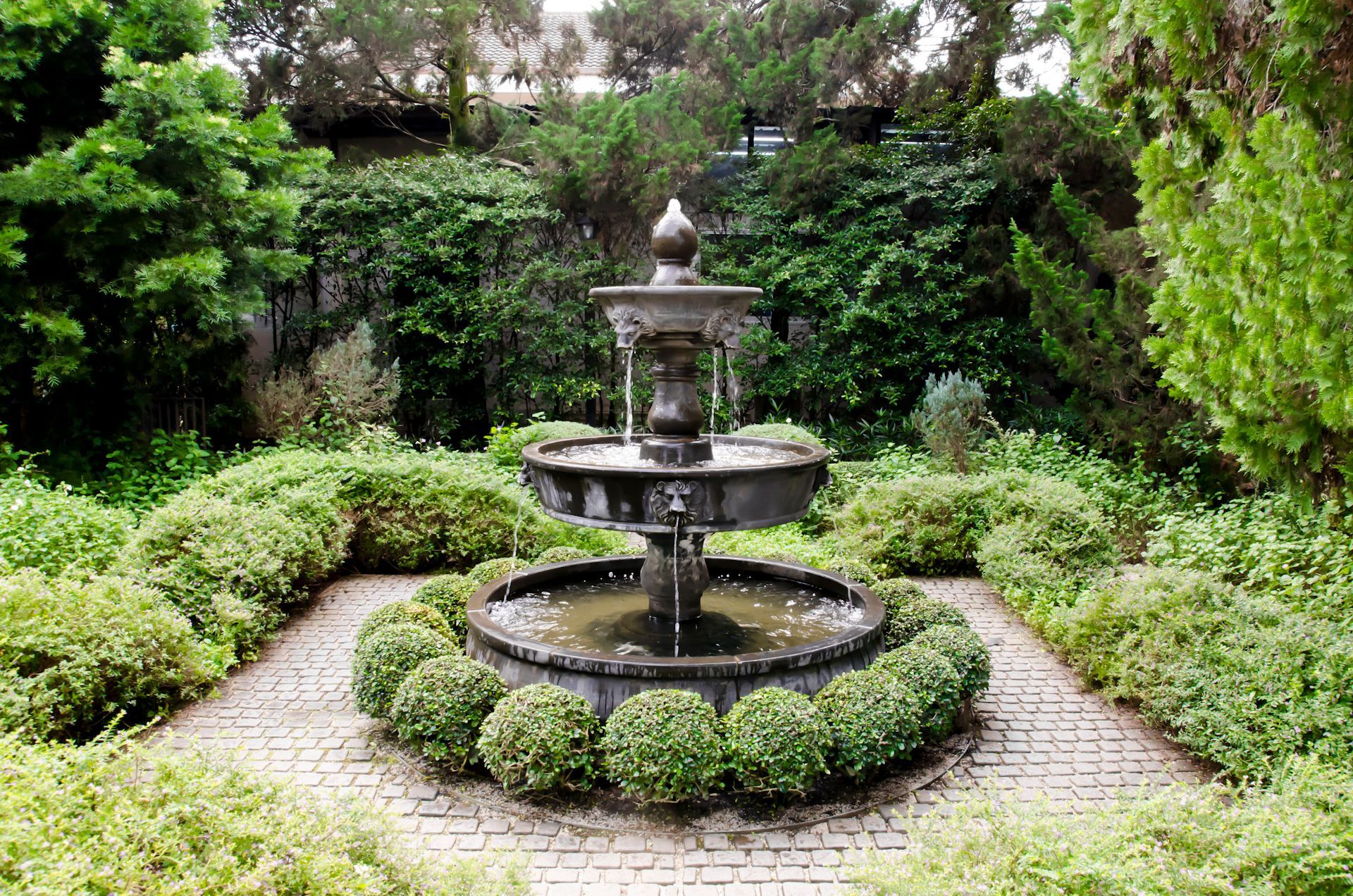 A fountain is surrounded by bushes and trees in a garden.