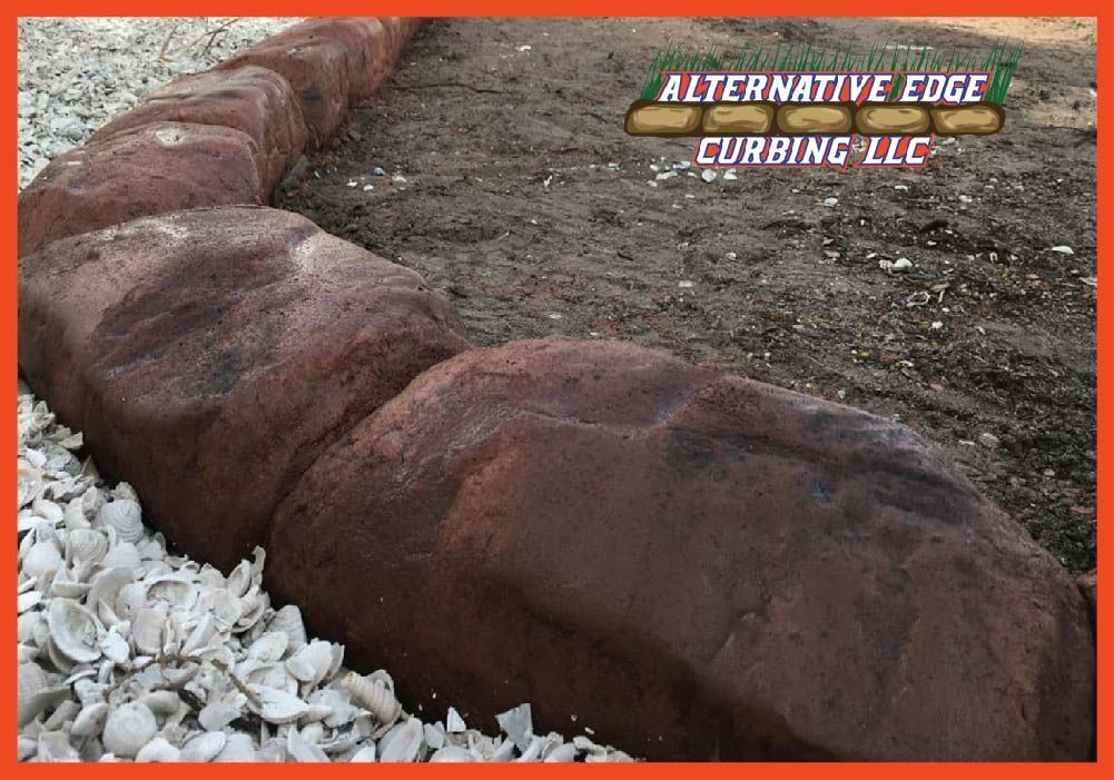 Brown rock-like edging borders a garden bed filled with dirt. White stones on the left.