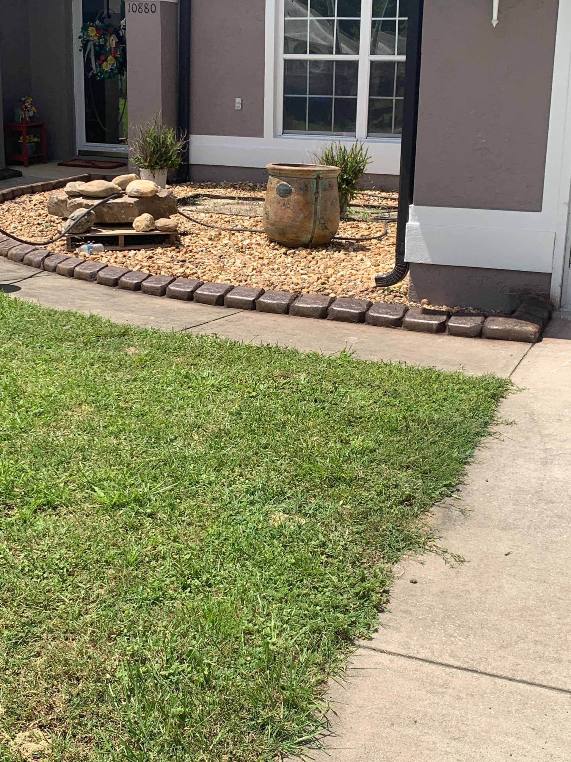 Lawn with a concrete path leading to a front yard with a rock garden and fountain.