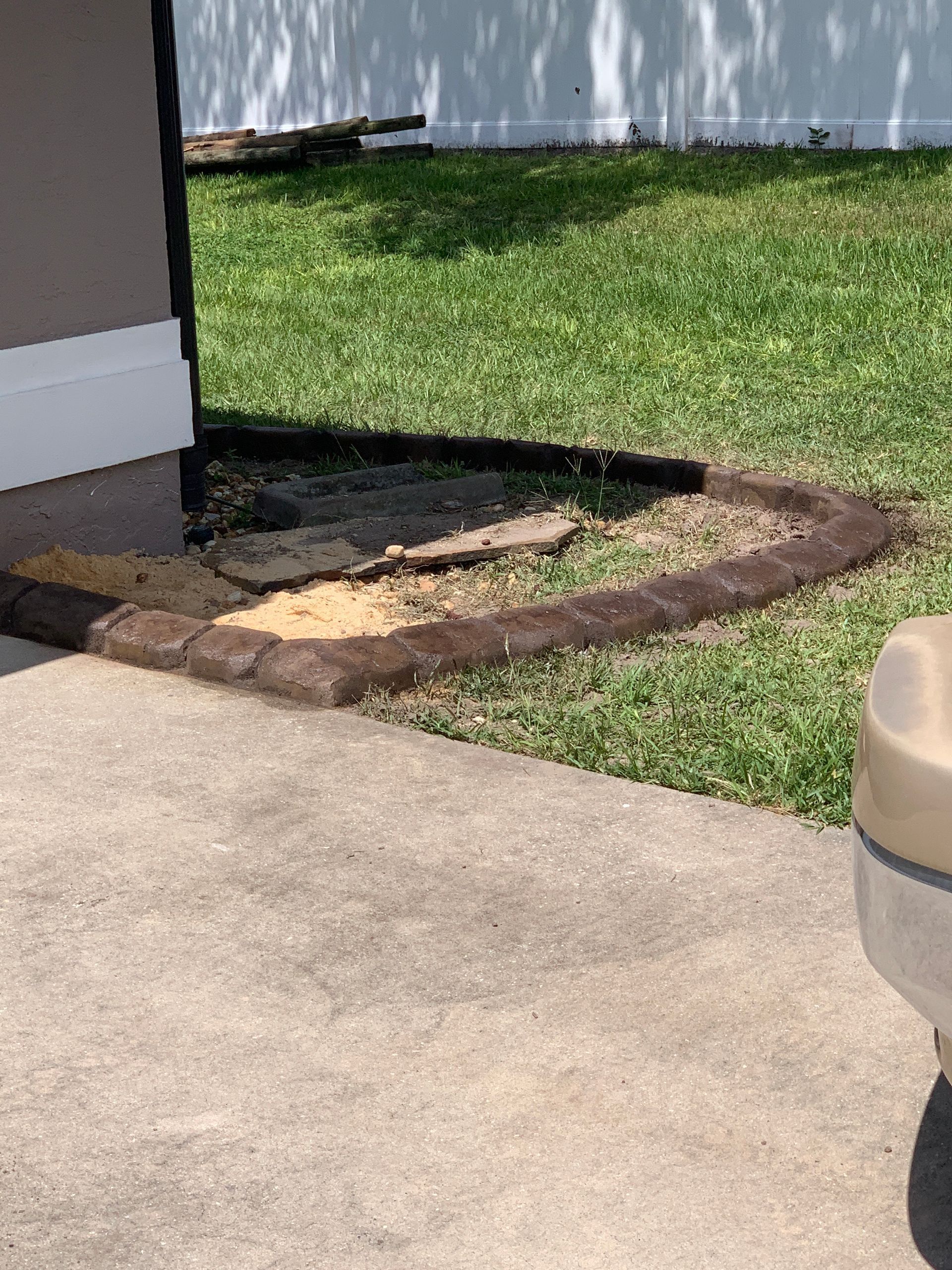 Concrete border around a dirt patch next to a building and grass lawn.