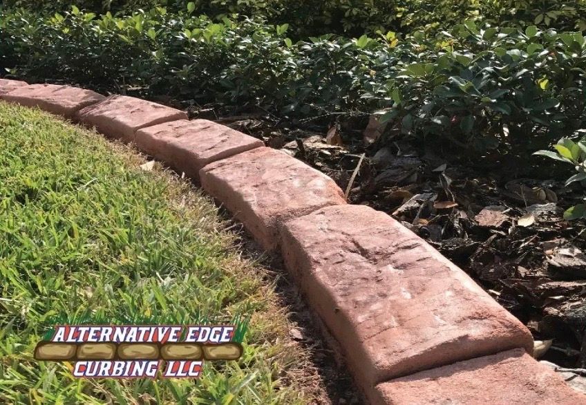 Red brick-style curbing separates green grass from a mulch-covered garden bed. 