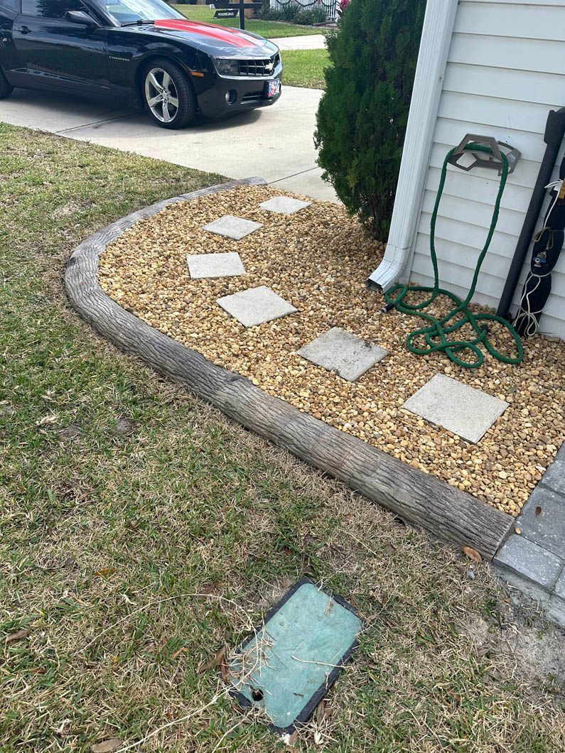 Landscaped yard with brown rocks, stepping stones, and a black car parked in front.