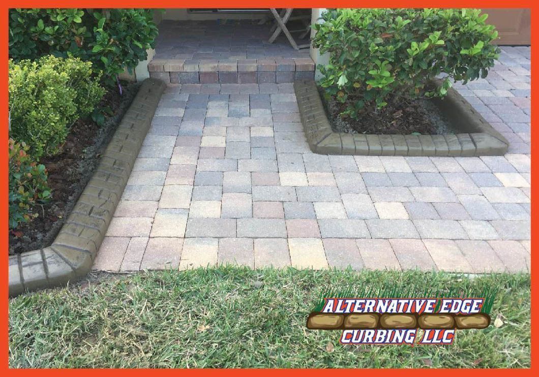Paved walkway with brick borders, planters, and grass. Text: Alternative Edge Curbing LLC.
