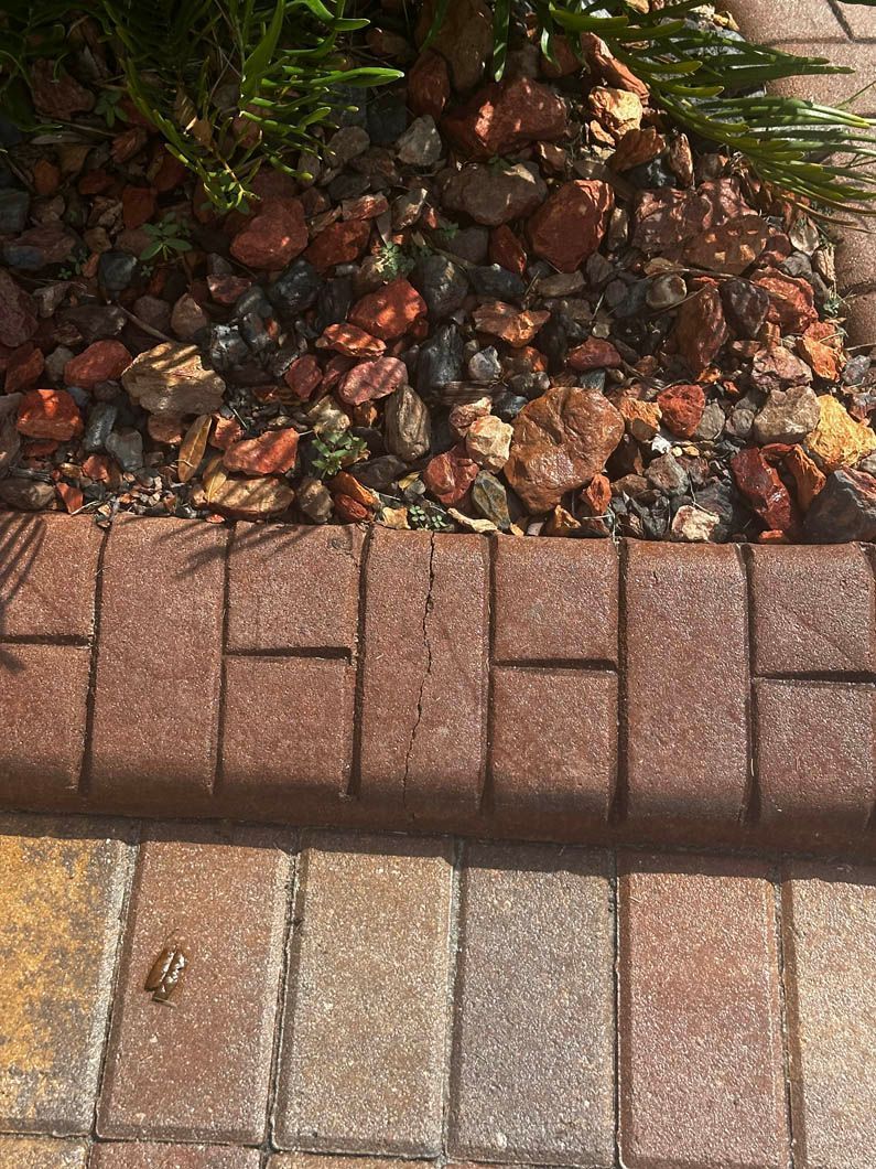 Gravel bed with red-brown rocks next to brown brick border and multi-color paving stones.
