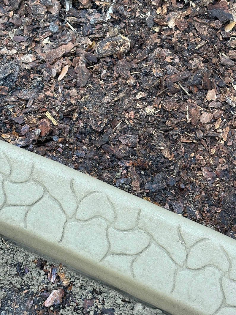 Beige stone-patterned edging borders dark mulch ground cover.
