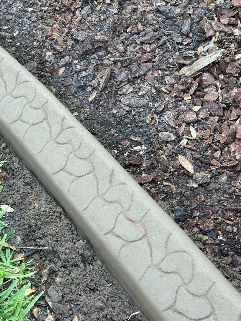 Concrete border with a cracked pattern next to mulch and grass.
