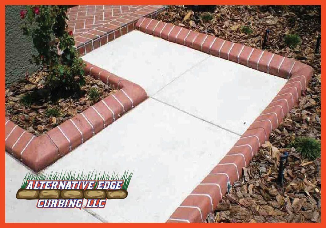 Red brick curbing borders a concrete pathway in a landscaped yard.