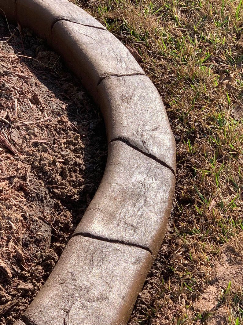 Curved brown concrete curbing separates dirt from grass.