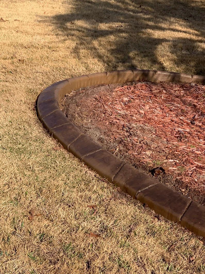 Brown concrete edging around a mulch-filled garden bed in a grassy yard.