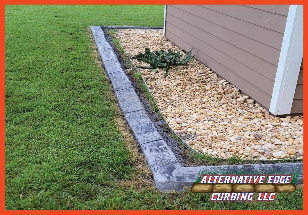 Concrete curbing separates grass from a rock-filled flower bed next to a building.