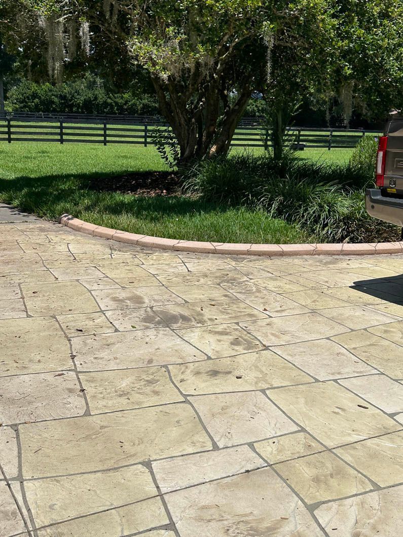 Stamped concrete driveway curving around a small, grassy area with a tree.