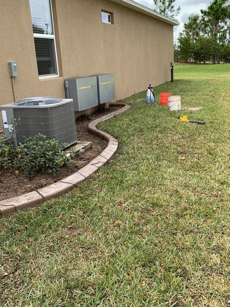 AC units near a tan building with a decorative border, grass, and gardening tools outside.