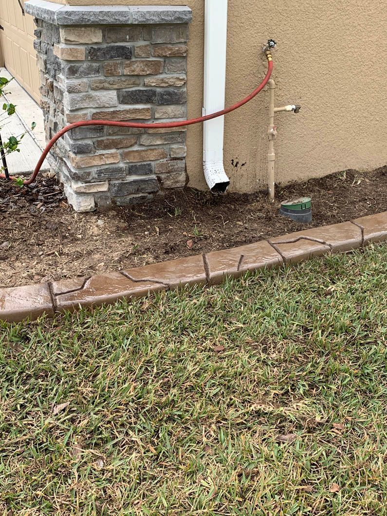 Exterior view: a water hose connected to a spigot on a house wall, next to a decorative stone border.
