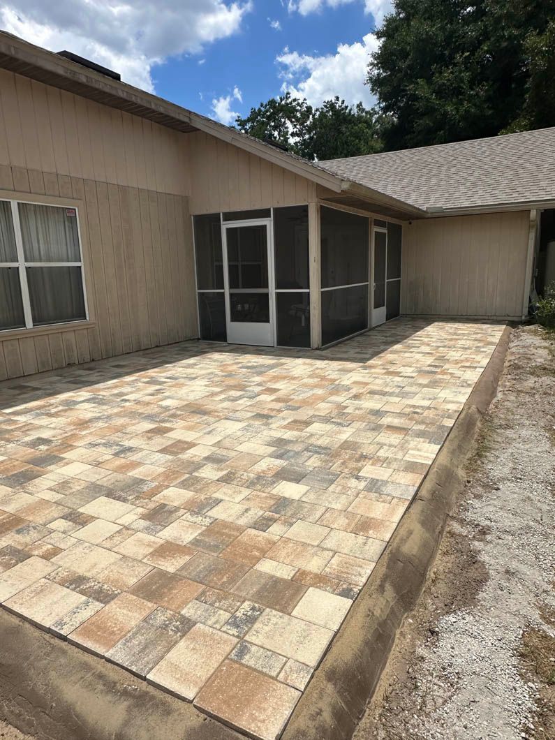 Patio with brick pavers extending from a screened porch, adjacent to a stucco home.