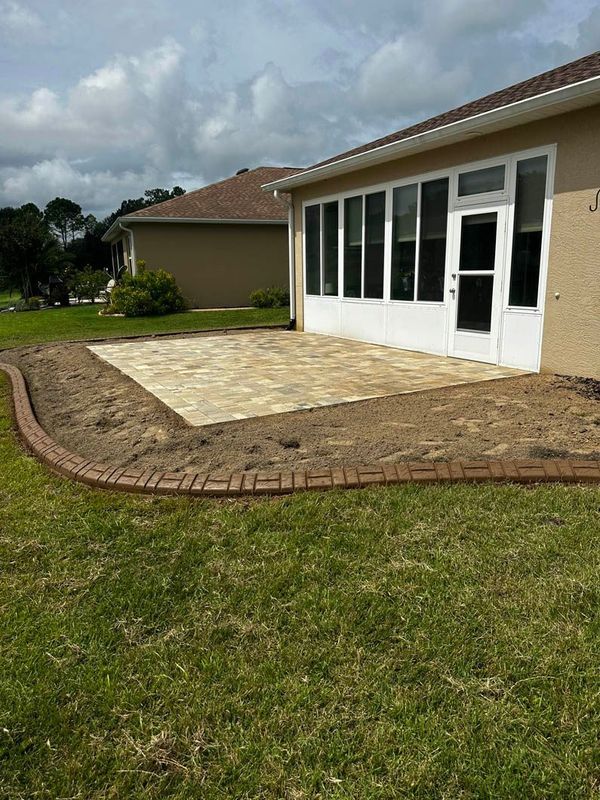 Paver patio bordered by brick edging next to a house with large windows and a green lawn.