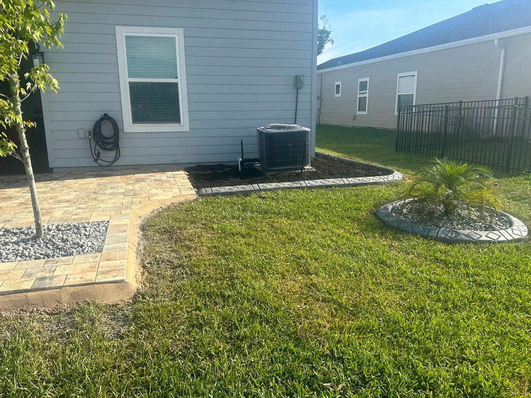 Backyard with blue house, AC unit, gravel borders, grass, and a small tree.