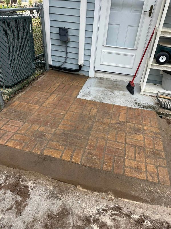 Brick patio with concrete near a blue building's white door. A red broom leans against the wall.