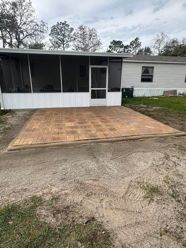 A brick patio outside a mobile home. A screen porch adjoins the house.
