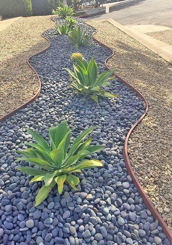 Landscaped garden bed with agave plants and dark gray river rocks.