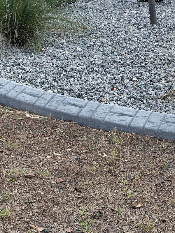 Gray concrete edging separates gravel from dirt and grass.