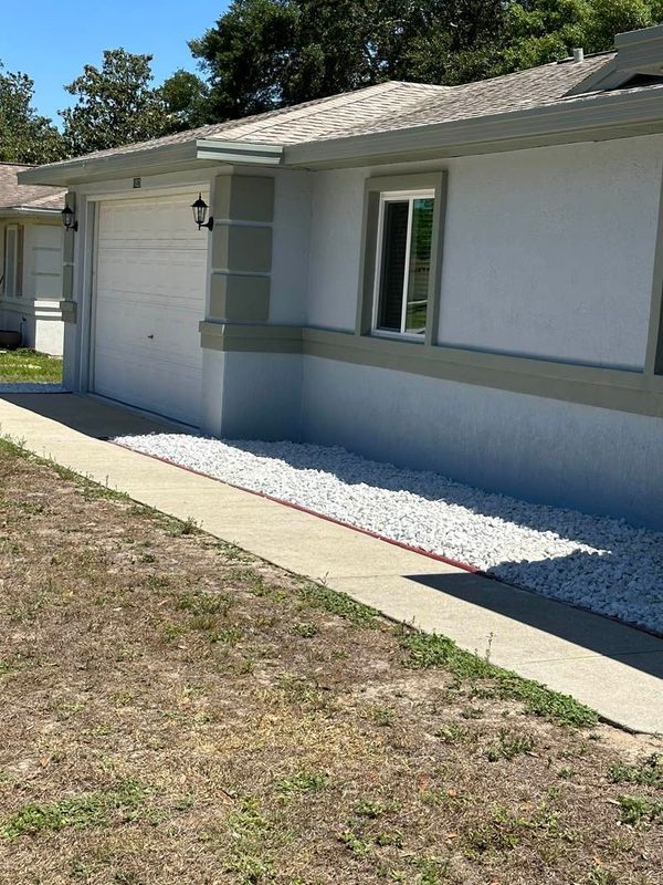 A light-colored house with a driveway, sidewalk, and rock landscaping.