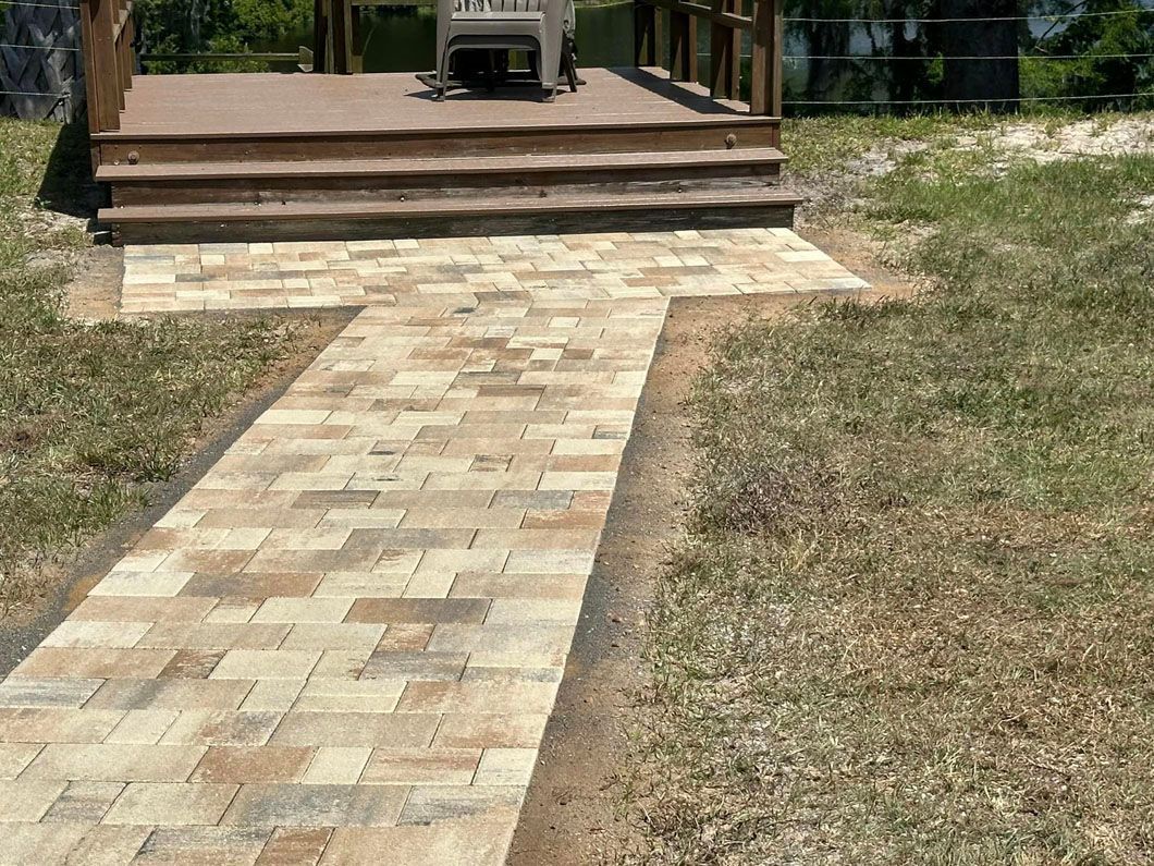 Brick pathway leading to wooden deck with steps, in a grassy outdoor setting.