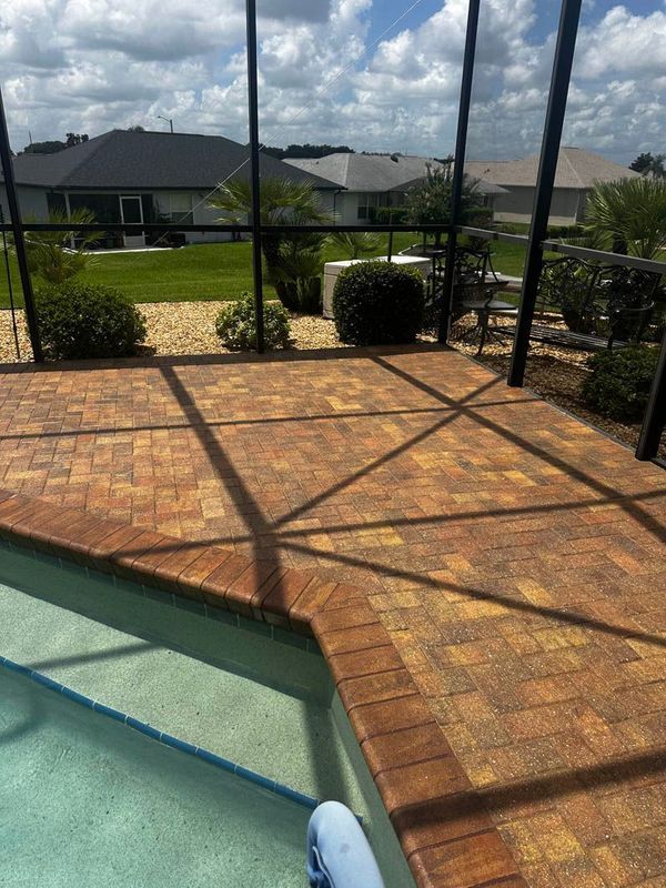 Brick patio with pool, surrounded by black screen enclosure; sunny day, residential area.