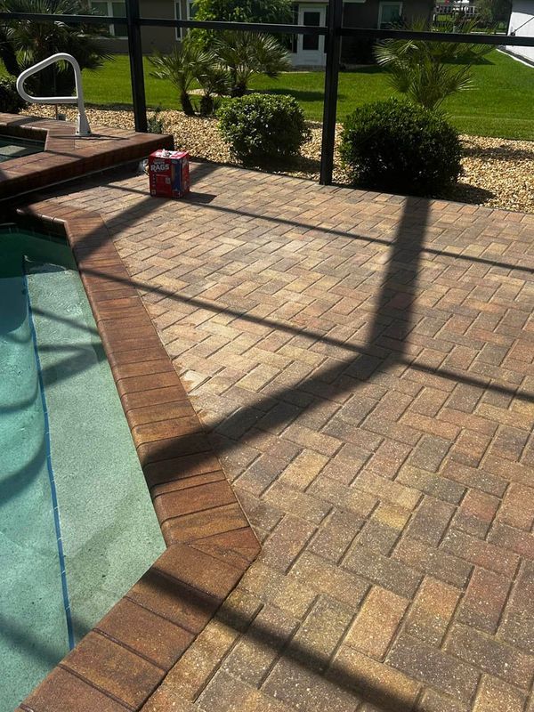 Brick patio around a pool, with a black shadow from a screen enclosure.