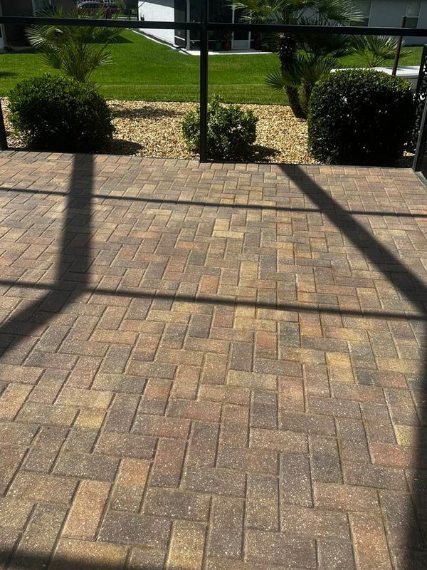 Brick patio with various colored bricks, with a view of a lawn, bushes, and a screen.